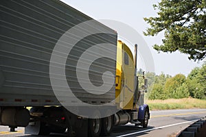 Yellow big rig classic American semi truck transporting perishables food in refrigerated semi trailers