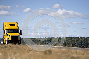 Yellow big rig semi truck tractor with day cab driving on the road along the river