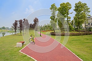 Yellow bike on lakeside red path in lawn along fenced houses in