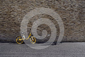 Yellow bike for rent on blacktopped way before grey stone wall in morning photo