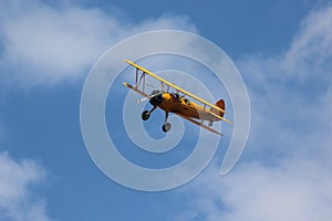 Yellow Biplane Flying in Blue Sky and Clouds