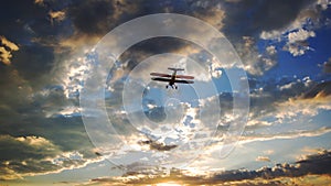 Yellow biplane flying into a cloudy sky at sunset