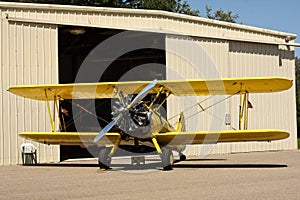 Yellow biplane in front of hangar