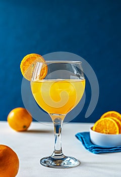 Yellow bird cocktail with rum, orange and lime juice, oranges, blue napkin. White table. Dark blue background.