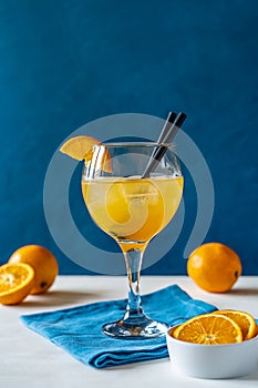 Yellow bird cocktail with rum, orange and lime juice, oranges, blue napkin. White table. Dark blue background.