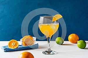 Yellow bird cocktail with rum, orange and lime juice, oranges and limes, blue napkin. White table. Dark blue background
