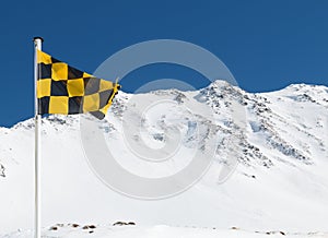 Yellow and black avalanche risk warning flag flying in the mount