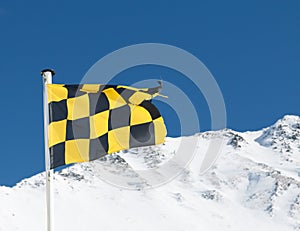 Yellow and black avalanche risk warning flag flying in the mount