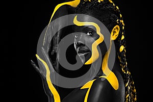 Yellow and black body paint. Woman with face art. Young girl with colorful bodypaint. An amazing afro american model