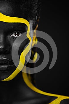 Yellow and black body paint. Woman with face art. Young girl with colorful bodypaint. An amazing afro american model