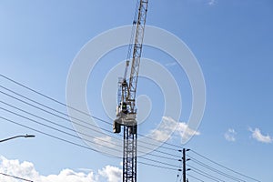 Yellow and black construction crane lifting load near power lines - blue sky with clouds