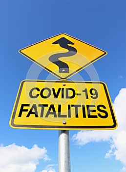 A yellow and black COVID-19 Fatalities warning sign with curvy upward arrow in a blue sky
