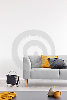 Yellow and black cushion on grey sofa in white loft interior with table and copy space. Real photo