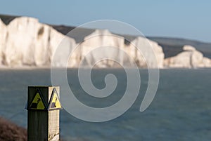 Yellow and black danger sign warning of erosion at the cliff edge. In the background Seven Sisters chalk cliffs, Seaford UK.