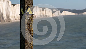Yellow and black danger sign warning of erosion at the cliff edge. In the background Seven Sisters chalk cliffs, Seaford UK.