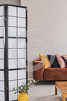 Yellow, black and pastel pink pillow on brown couch in grey living room interior, copy space on empty wall