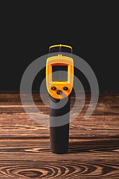Yellow-black pyrometer on a wooden background. A device for non-contact temperature measurement