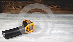 Yellow-black pyrometer on a wooden background. A device for non-contact temperature measurement