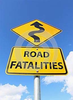 A yellow and black Road Fatalities sign with curvy upward arrow in blue sky