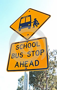 Yellow and black school bus stop ahead sign and blue sky