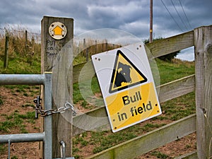 A yellow and black sign fixed to a wooden fence warns walkers of a bull loose in a field ahead