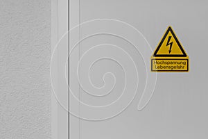 Yellow and black sign with the text danger high voltage on a white metal door with copy space