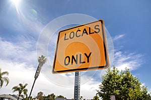 Yellow and black square road sign in neighborhood reading Locals Only against a blue sky