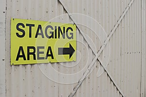 a yellow and black Staging Area sign with arrow on the corrugated iron door at an airport