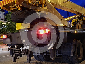 A yellow-black truck crane with headlights on stands on a night road. Road works