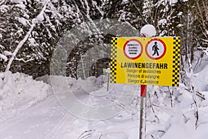 Yellow black warning sign and signs in German, English, Italian and French: Closed, Danger of avalanche. Snow-covered forest