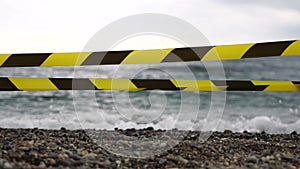 Yellow black warning tape barrier ribbon swinging in the wind across exotic sea beach background without people. No