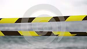 Yellow black warning tape barrier ribbon swinging in the wind across exotic sea beach background without people. No