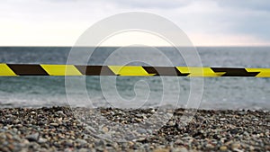 Yellow black warning tape barrier ribbon swinging in the wind across exotic sea beach background without people. No