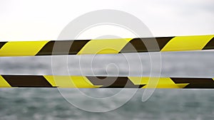 Yellow black warning tape barrier ribbon swinging in the wind across exotic sea beach background without people. No