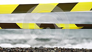 Yellow black warning tape barrier ribbon swinging in the wind across exotic sea beach background without people. No