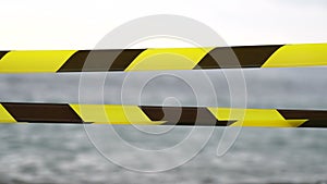 Yellow black warning tape barrier ribbon swinging in the wind across exotic sea beach background without people. No