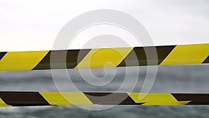 Yellow black warning tape barrier ribbon swinging in the wind across exotic sea beach background without people. No