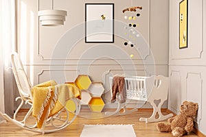 Yellow blanket on white wooden rocking chair in spacious baby bedroom with teddy bear and rug on the floor