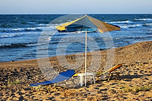 Yellow-blue beach umbrella and sun beds with table on a sandy beach by the sea