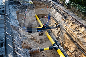 Yellow, blue, black plastic pipes and cables in an excavated trench.