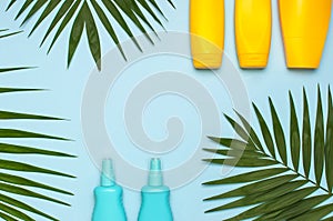 Yellow and blue bottles of sunscreen cream, tropical palm leaves on bright blue background top view flat lay copy space. Sun