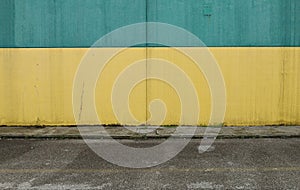 Yellow and blue painted concrete wall with worn sidewalk and street in front