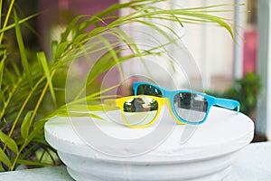 Yellow and blue sunglasses on white terrace over blurred pink house background.