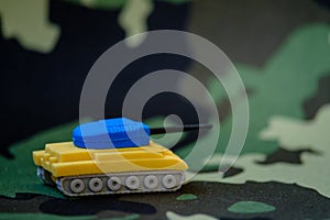 Yellow-blue tanks figures on camouflage background, Ukrainian flag colors on toy tank figures, anti-war concept