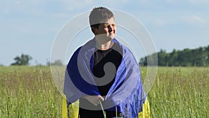 The yellow-blue Ukrainian flag in the hands of a boy walking against the background of a green field. Child with the
