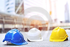 Yellow, blue and white hard safety wear helmet hat in the project at construction site building on concrete floor on city.