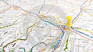 A yellow board pin stuck in Bologna on a map of Italy