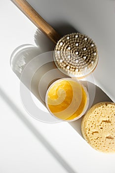 Yellow body scrub, dry massage anti-cellulite brush and sponge on white background
