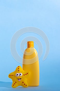 A yellow bottle with children's cosmetics with a place for a logo and funny toy on a light blue background. Copy
