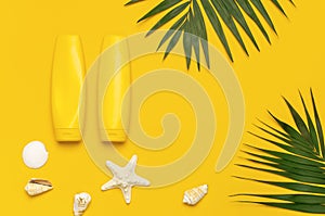 Yellow bottles of sunscreen cream, tropical palm leaves, shells, starfish on bright yellow background top view flat lay copy space